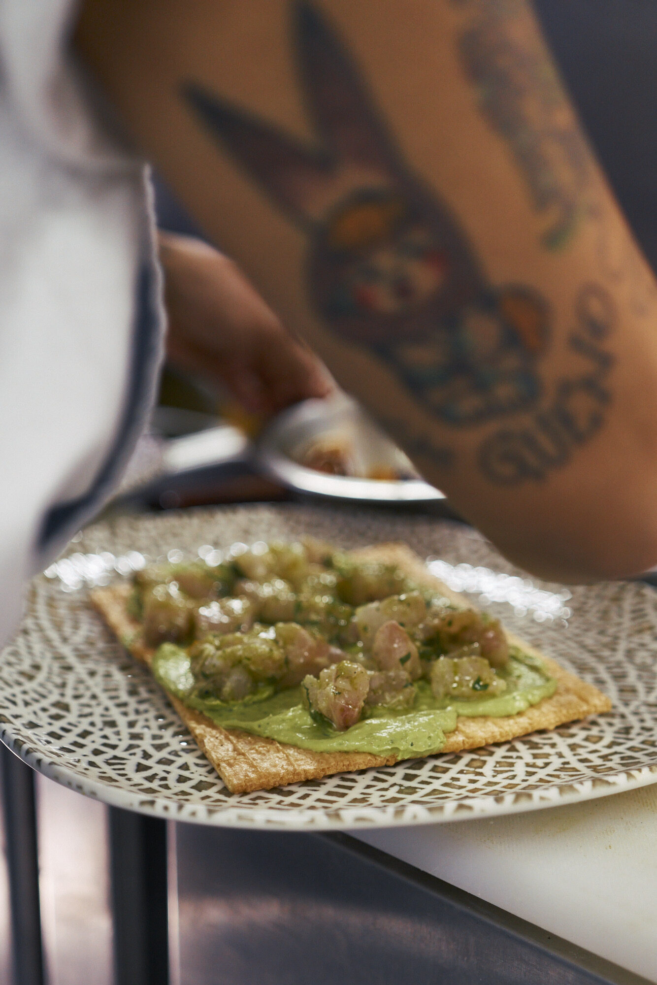 Manos tatuadas emplatando una tostada de ceviche